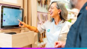 Profissional sorridente atendendo cliente em loja com tela digital interativa, simbolizando o uso de tecnologia para aprimorar a experiência do consumidor.