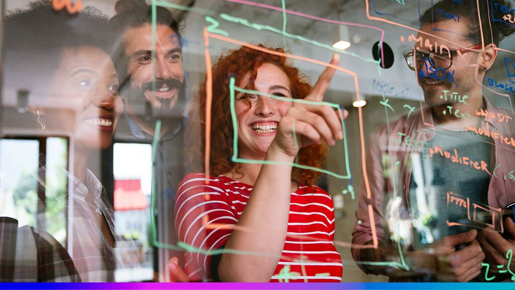 Equipe de profissionais planejando um mapa de jornada do cliente em um quadro de vidro com anotações coloridas, representando o design de experiências omnichannel.