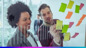 Profissionais planejando estratégias de retenção com post-its coloridos em um quadro de vidro, simbolizando o desenvolvimento de ações para fidelizar clientes enterprise.