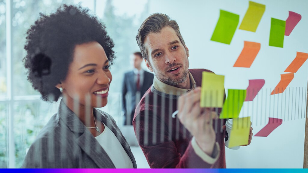 Profissionais planejando estratégias de retenção com post-its coloridos em um quadro de vidro, simbolizando o desenvolvimento de ações para fidelizar clientes enterprise.