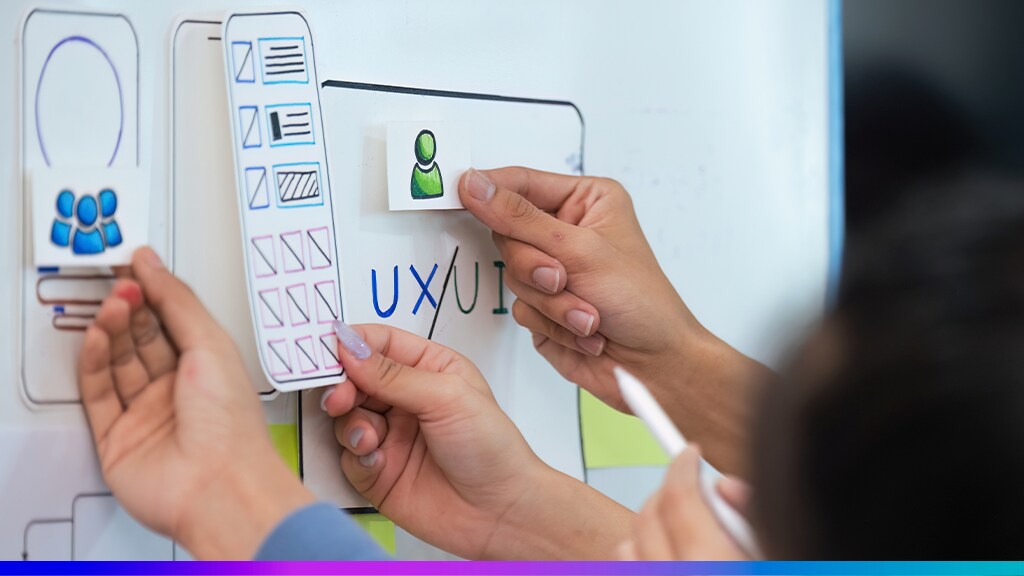 Equipe ajustando elementos visuais e ícones em um quadro com a palavra UX/UI, simbolizando a aplicação de boas práticas de design de experiência do usuário.