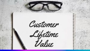 Caderno com a frase “Customer Lifetime Value”, caneta e óculos sobre a mesa, representando o conceito de valor vitalício do cliente nas estratégias empresariais.