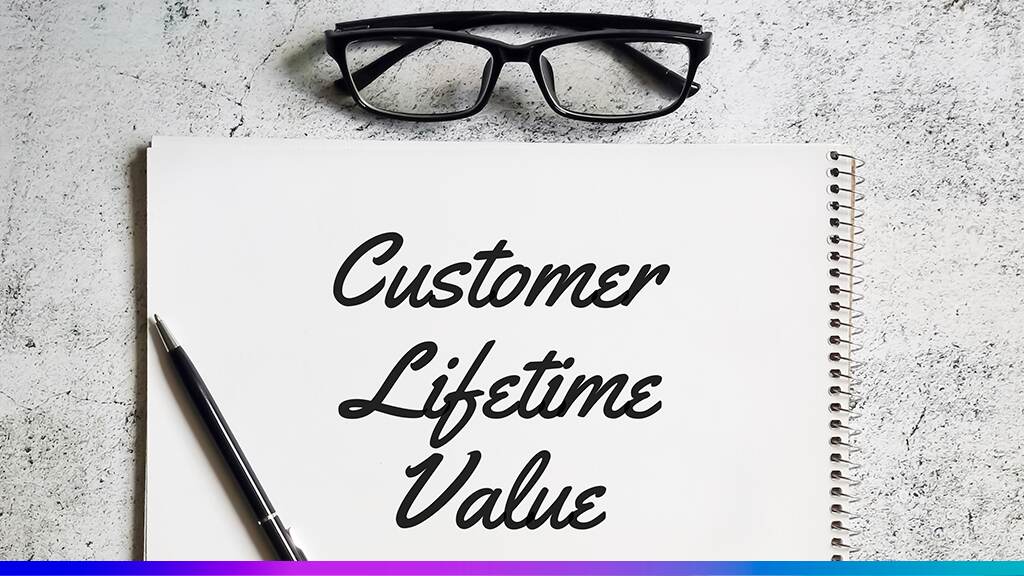 Caderno com a frase “Customer Lifetime Value”, caneta e óculos sobre a mesa, representando o conceito de valor vitalício do cliente nas estratégias empresariais.
