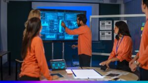 Profissionais em sala escura observando painel digital com gráficos e dados de desempenho em tempo real.