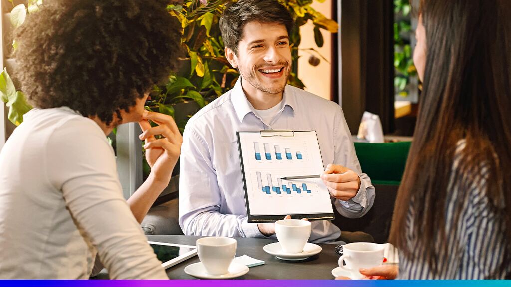 Homem apresentando relatório de gráficos em reunião com colegas em um café, simbolizando estratégias de retenção de clientes.