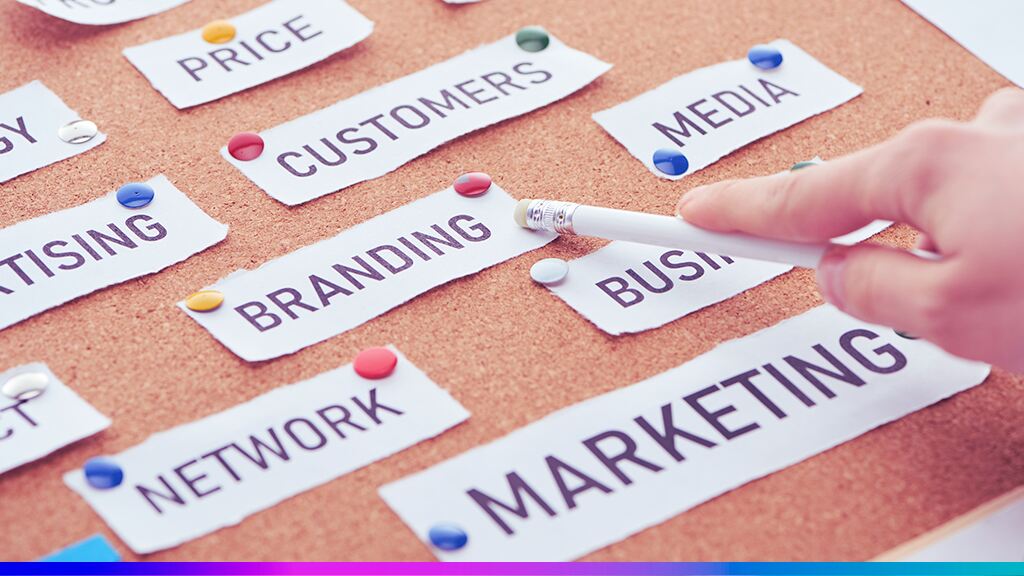 Palavras relacionadas ao marketing presas em um quadro de cortiça, destacando termos como “branding”, “customers” e “media”, representando integração de estratégias de marketing.